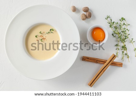 Traditional Italian soup in a large white plate with fields and ingredients - egg yolk, cinnamon sticks, thyme, and nutmeg