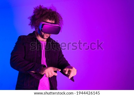 Metaverse concept. Hipster young man using virtual reality headset over blue purple background. Concept of hi tech and modern technology. 