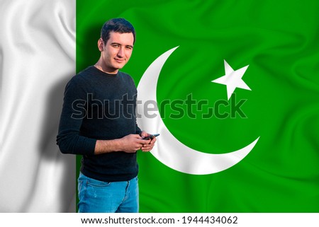 Pakistan flag on the background of the texture. The young man smiles and holds a smartphone in his hand. The concept of design solutions.