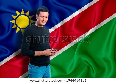 Namibia flag on the background of the texture. The young man smiles and holds a smartphone in his hand. The concept of design solutions.