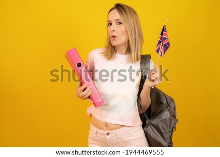 Beautiful blonde woman with the flag of Great Britain over yellow background.