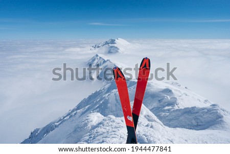 Red ski in winter season, mountains and ski touring equipments on the top in sunny day. Alps above the clouds. Winter vacations. Snowy mountain background