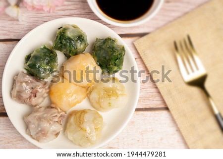 Steamed Dumplings stuffed with sliced garlic chives or leeks, chopped taro, bamboo shoots and cabbages dipping with special soy sauce serving on white plate. It is called "Kui Chai" in Thailand