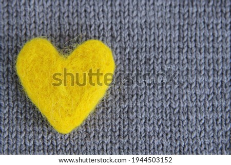 A yellow heart made of wool lies on a gray knitted background.The concept of handmade, needlework, Valentine's day.The colors of 2021 are gray and yellow. Top view.Flat styling style.Copyspace