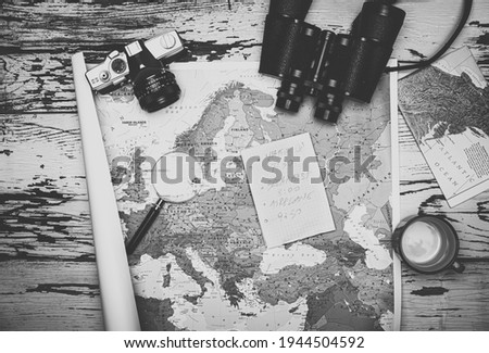 Flat lay of the travel planning concept. Top view in black and white of a note paper, binoculars, and Europe map on a wooden table