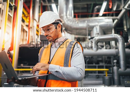 Professional worker of modern factory using laptop controlling program to automatic machinery. Engineering with laptop Programmable Logic Controller to manage large machine working full automatic. Royalty-Free Stock Photo #1944508711