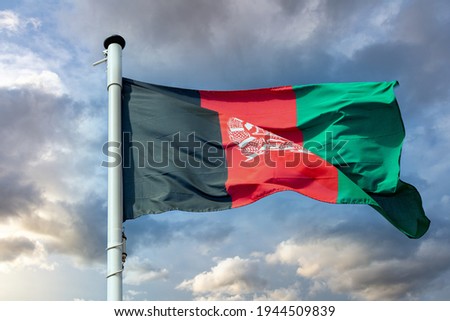 Afghanistan sign symbol. Afghani national flag on a pole waving against cloudy sky background.