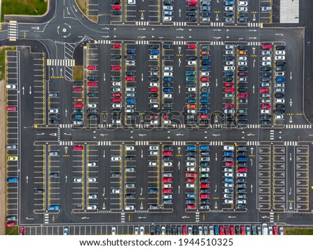Busy large modern carpark with symmetrical roads rows of parking bays lots of symmetry and colours aerial view from drone up above looking down on tarmac asphalt car storage 