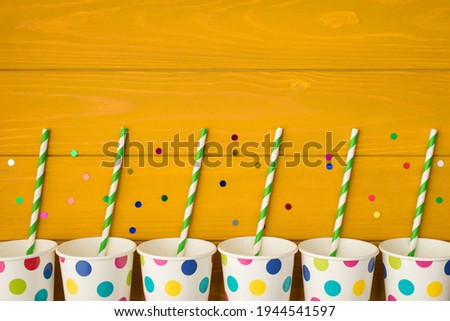 Overhead photo of cups drink with party tubules and multicolored confetti isolated on the yellow wooden background with empty space