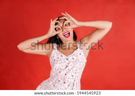 Cheerful female  showing Ok gestures with both hands, pretending to wear spectacles, and smiling broadly, enjoying her carefree happy life