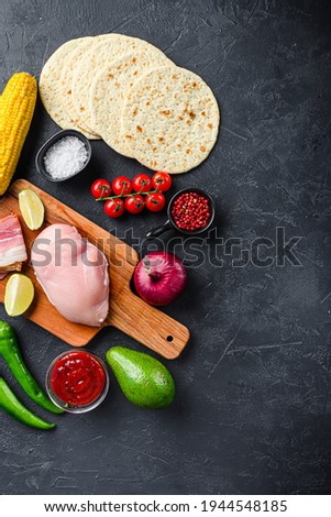 Raw organic ingredients for tacos with chicken meat, corn tortilla, salsa, chilli over black background, top view with space for text