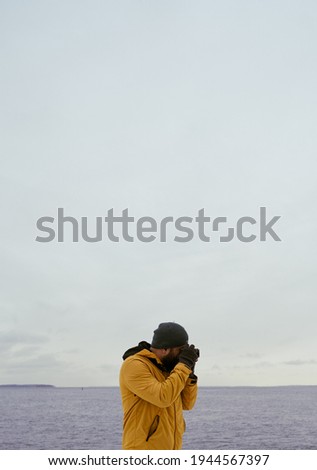 Man wearing a yellow jacket taking a photo in front of the ocean