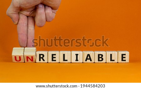 Unreliable or reliable symbol. Businessman turns wooden cubes and changes the word unreliable to reliable. Beautiful orange background, copy space. Business and unreliable or reliable concept. Royalty-Free Stock Photo #1944584203