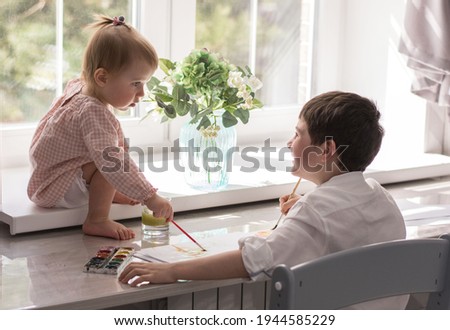 children sit on the table and draw with watercolor