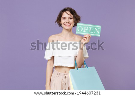 Smiling young woman girl in summer clothes isolated on violet wall background studio portrait. Shopping discount sale concept. Mock up copy space. Hold package bag with purchases sign with OPEN title