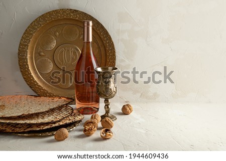 Golden plate for Seder Pesach (Jewish Passover holiday)  (with the inscriptions: egg, shankbone, bitter herbs, lettuce, charoses, parsley) Wine bottle, round matzo on a vintage plate, glass, walnuts.  Royalty-Free Stock Photo #1944609436