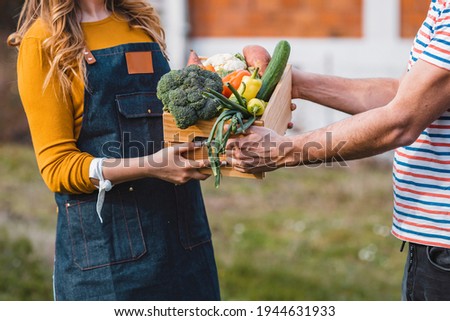 Organic local farmer giving veggies to shopper outside. Home Delivery Of Fresh Produce Outside House Observing Safe Social Distancing During Coronavirus Covid-19 Pandemic