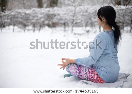 A back view on a woman who practices outdoor yoga. Tranquil state of mind. A sitting girl on snowy background.