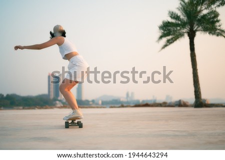 Asian Beautiful women surf skate or skateboard outdoors on beautiful summer day. Happy young women play surf skate at park near the beach on morning time. Sport activity lifestyle concept. Royalty-Free Stock Photo #1944643294