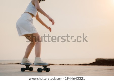 Close-up Asian Beautiful women surf skate or skateboard outdoors on beautiful summer day. Happy young women play surf skate at park near the beach on morning time. Sport activity lifestyle concept. Royalty-Free Stock Photo #1944643321