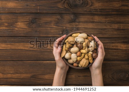 Women's hands with a bowl filled with nut mixture on a wooden rustic table. Vegetarian food.