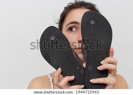 Woman with pair of black slippers in front of her face on white background
