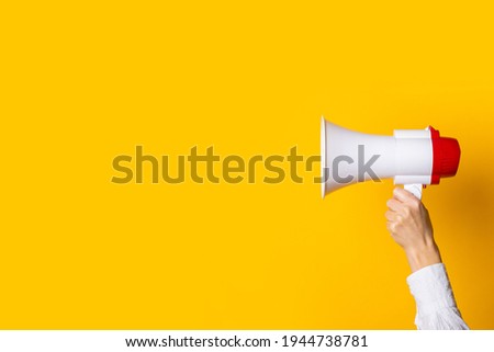 female hand holds a white with a red megaphone on a yellow background