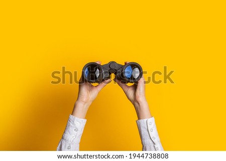 female hands hold black binoculars on a bright yellow background. Royalty-Free Stock Photo #1944738808