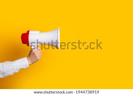female hand holds a white with a red megaphone on a yellow background