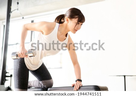 Asian woman doing one-handed rowing in a training gym Royalty-Free Stock Photo #1944741511