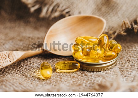 Fish oil capsules on a wooden spoon. Fish oil pills, tablets on the burlap. Vitamin complex omega 3,6,9. Fish oil capsules with omega-3, vitamin D. Close up