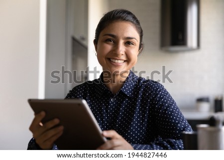 Head shot portrait smiling Indian young woman holding tablet in hands, happy businesswoman or student using gadget, surfing internet, female support operator ready to consulting client online