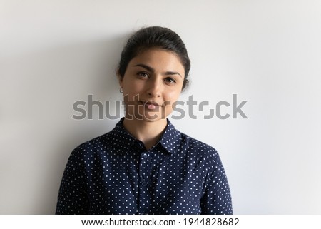 Head shot portrait attractive young Indian woman looking at camera, standing on white wall studio background isolated, confident millennial businesswoman or student posing for photo, profile picture