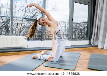 Girl in grey pants and top stand on knees at mat, bend and stretch back, raise hand up with closed eyes and flying hair, enjoying sport activity