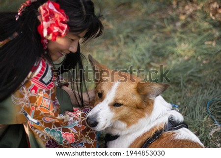 A beautiful Japanese woman in a traditional flower kimono clothes looks at a dog. A smiling model with a dog on light green background. Happy friendship connection.