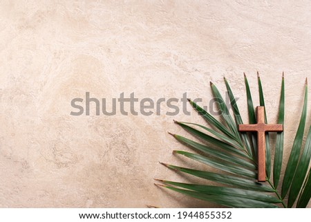 Palm Sunday concept. Wooden cross over palm leaves. Reminder of Jesus sacrifice and Christ resurrection. Easter passover. Eucharist concept. Christianity symbol and faith.