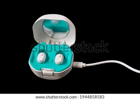Hearing aid in a case with a charging cable on a black background. Space for your design. Royalty-Free Stock Photo #1944858583