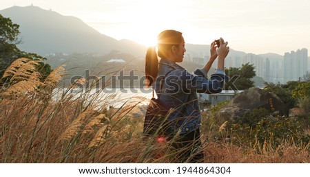 Woman uses mobile phone to take photos at sunset 