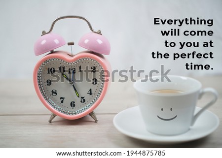 Inspirational motivational quote - Everything will come to you at the perfect time. With a happy smile sign on white cup of coffee and alarm clock on white table bright background.