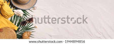 Woman's beach accessories: swimsuit, bikini, rattan bag, straw hat, shells, sunglasses, palm leaves on sand background. Exotic, tropical mood. Summer vacation, travel concept. Flat lay. Copy space.