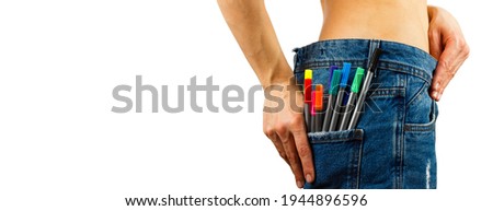 Slim body in blue jeans with colored felt tip pen in the pocket, light background