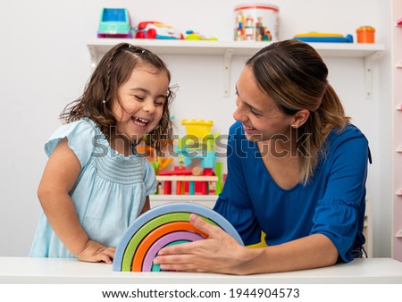 Two-year-old girl and her young kindergarten teacher, both Caucasian, play together in kindergarten, smiling happily Royalty-Free Stock Photo #1944904573