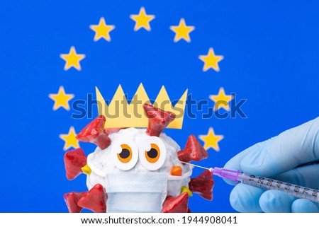 Handmade cell of Covid-19 virus in front of flag of European Union and a hand with syringe making an injection to it. Vaccination in Europe concept