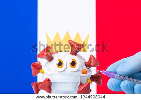 Handmade cell of Covid-19 virus in front of flag of France and a hand with syringe making an injection to it. Vaccination in France concept
