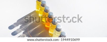Vials of colored liquid are arranged in a row. Curly shadows fall on a white background.