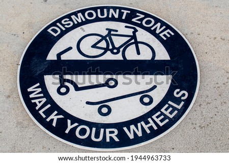 Round blue and white Dismount Zone - Walk Your Wheels sign painted on sidewalk - Grungy and view from top