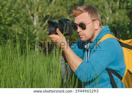 The photographer holds a professional photo-video camera in his hands. Against the backdrop of green nature and forest