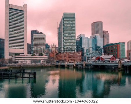 Boston City Skyline at Dusk. Pink Sky and Bright Sunrays over Blue Water Reflections. Peaceful Scenery over the Boston Harbor Boardwalk.
