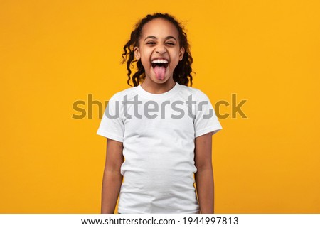 Naughty black teenage girl with curly hair misbehaving, showing sticking out her tongue at camera as a sign of disobedience, protest and disrespect. Human emotions, reactions, feelings and attitude