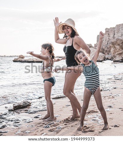 A young mother and two little daughters are having fun, dancing and laughing on the seashore. Happy family on vacation.